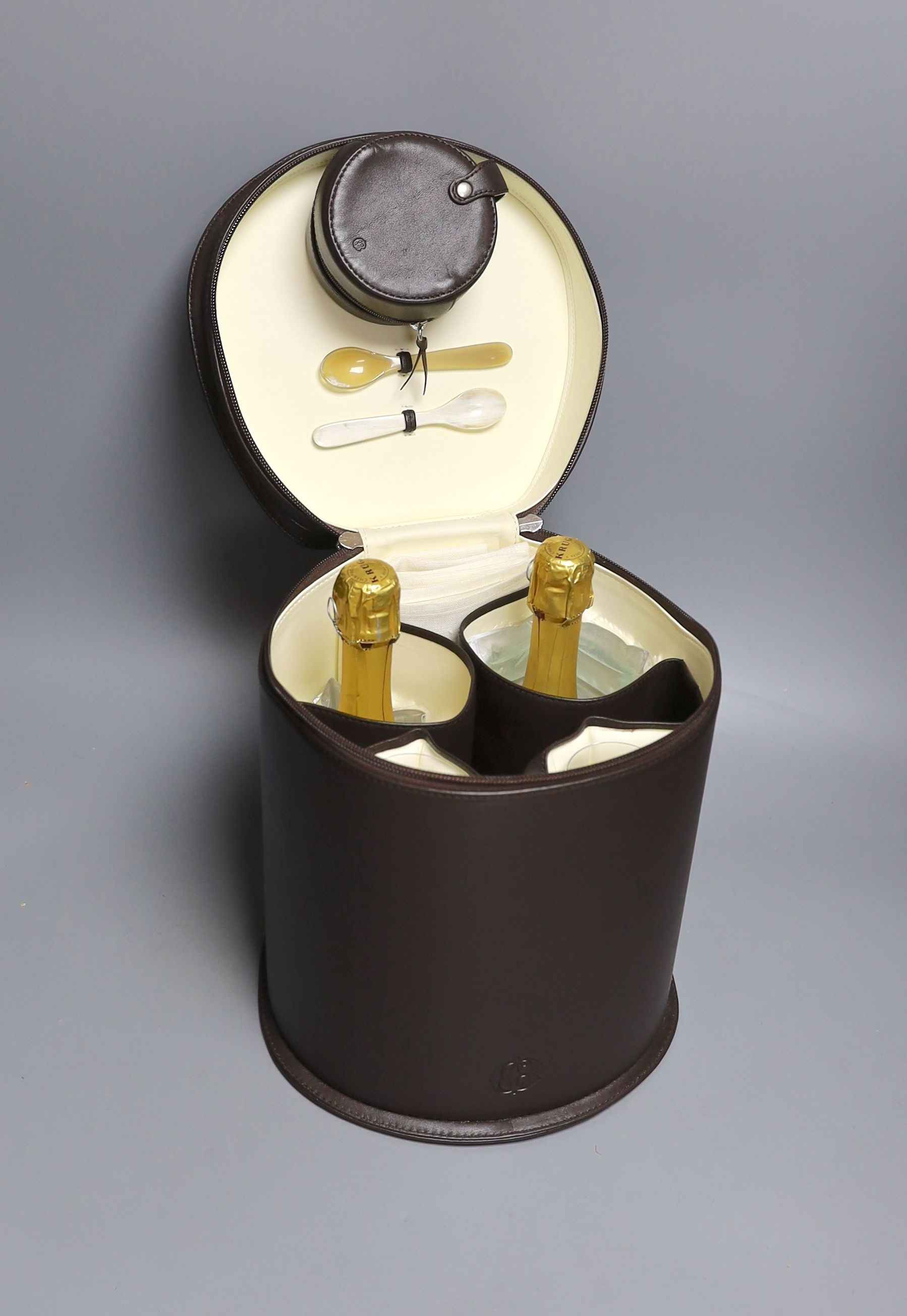 A Connolly leather Krug champagne carrier with dust cover, containing: two half bottles, two champagne chillers, two Krug champagne flutes, two Connolly linen napkins, a leather caviar pouch and two bone caviar spoons